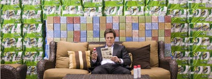 Paul Morgan Played By Hugh Grant, Sat In The Middle Of A Sofa Looking At A Magazine