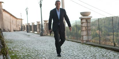 Jack Played By George Clooney, Walking Down A Path Holding A Gun