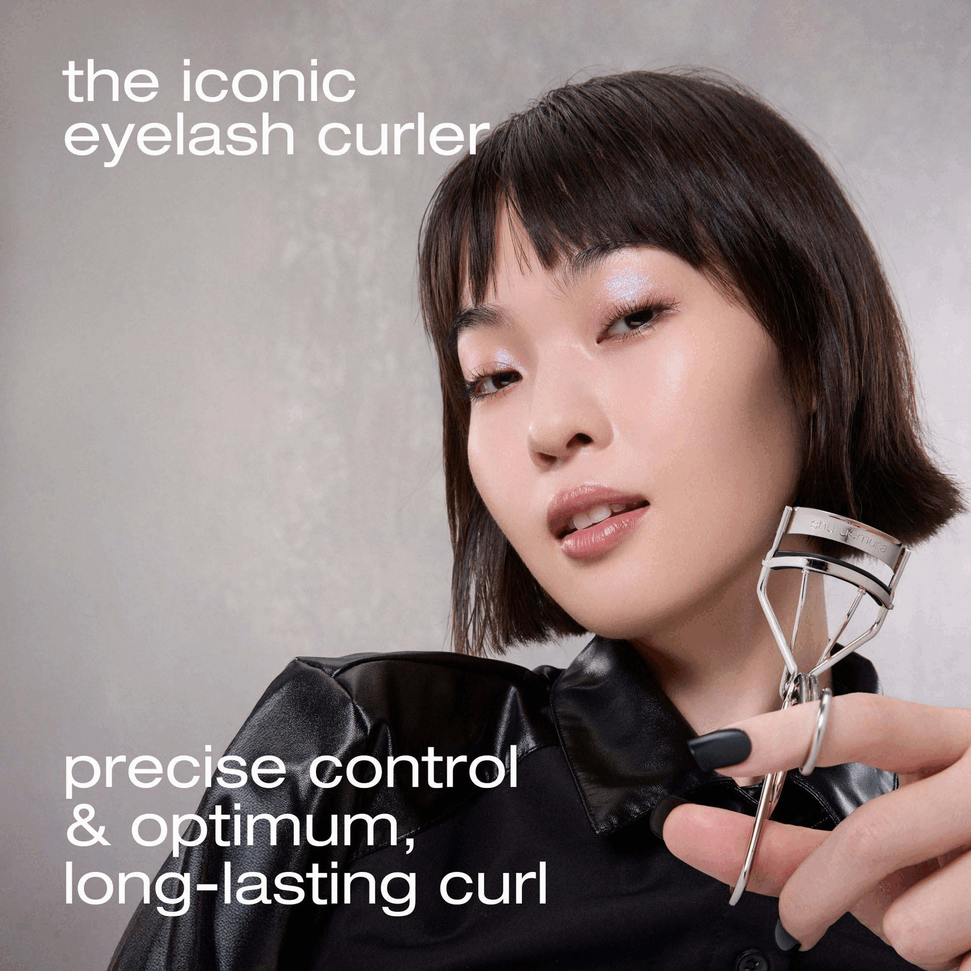 Image 1 - A model holds a Shu Uemura eyelash curler near her face, with text that reads the iconic eyelash curler and precise control & optimum, long-lasting curl. 
Image 2 - Close-up of a metallic eyelash curler with a black rubber pad against a grey background with the text comfortable curl thanks to the flatter curve that gently hugs eye shapes. 
Image 3 - A close-up of a shiny chrome eyelash curler with a black pad and text high-quality silicone rubber pads for a gentle effective curl without tugging or pulling shu uemura. 
Image 4 - Close-up of a shiny metal hinge mechanism of a beauty tool on a grey background with the text precisely engineered & extremely durable, the innovative hinge ensures stable pinch-free curl. 
Image 5 - A close-up view of an eye with shiny sparkly eyeshadow and dark eyelashes. 
Image 6 - A shiny silver Shu Uemura eyelash curler with the shu uemura logo on it, next to a red circular sticker that reads BEST OF BEAUTY allure THE BEAUTY EXPERT 2024 AWARD WINNER.