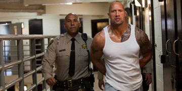 Driver Played By Dwayne Johnson Being Led Through Prison By A Guard
