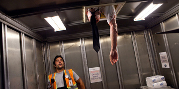 A Scared Man Stood In A Lift With Another Man trying To Get In Through The Door In The Roof