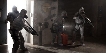 Four People In A Dark Room With Full Body Suits And Masks On With A Tourch And Guns
