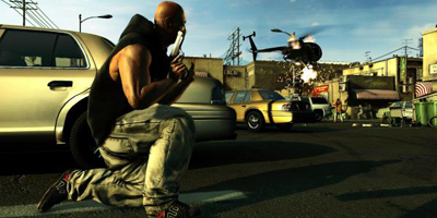 A player, crouching behind a car as a helicopter gets shot down in the background