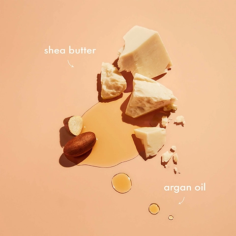 Image 1 - An arrangement of shea butter pieces and argan oil droplets on a soft peach background, with labels indicating shea butter and argan oil.