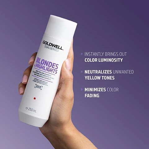 Image 1 - A hand holds a white Goldwell Dualsenses Blondes & Highlights Anti-Yellow Shampoo bottle against a purple background, with text on the right stating Instantly Brings Out Color Luminosity, Neutralizes Unwanted Yellow Tones, and Minimizes Color Fading. Image 2 - A white Goldwell Dualsenses Blondes & Highlights Anti-Yellow Shampoo bottle is displayed with a vibrant purple shampoo swatch, alongside text that reads Goldwell Dualsenses Blondes & Highlights Anti-Yellow Shampoo, Shampooing Anti-Reflets Jaunes, Anti-Gelbstich Shampoo, e 250 mL, The next generation of color luminosity, The new Luminescine technology transforms non-visible UV light into visible light for magnificent brilliance, MicroPROtec complex + FadeStopFormula + Luminescine = Superb color brilliance. Image 3 - A white bottle of Goldwell Dualsenses Blondes & Highlights anti-yellow shampoo stands upright on a purple background, with visible text reading GOLDWELL DUALSENSES BLONDES & HIGHLIGHTS ANTI-YELLOW SHAMPOO SHAMPOOING ANTI-REFLETS JAUNES ANTI-GELBSTICH SHAMPOO FÜR BLONDES HAAR FOR BLONDE HAIR CHEVEUX BLONDS COLOR LUMINOSITY e 250 mL, and below the bottle, ClimatePartner certified product climate-id.com/PBNVQ3 CO2 measure reduce contribute.