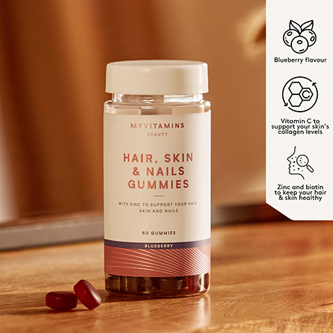 A bottle labeled MYVITAMINS BEAUTY HAIR SKIN & NAILS GUMMIES WITH ZINC TO SUPPORT YOUR HAIR SKIN AND NAILS 60 GUMMIES BLUEBERRY sits on a wooden surface with two gummies nearby next to a panel listing benefits Blueberry flavour Vitamin C to support your skins collagen levels Zinc and biotin to keep your hair & skin healthy.