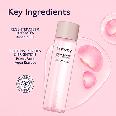 A By Terry Baume de Rose LEau Micellaire Micellar Water bottle stands on a clear surface with pink rose petals, alongside text that reads Key Ingredients, REGNERATES & HYDRATES Rosehip Oil, SOFTENS, PURIFIES & BRIGHTENS Pastel Rose Aqua Extract, and a circular badge with VEGAN FORMULA.