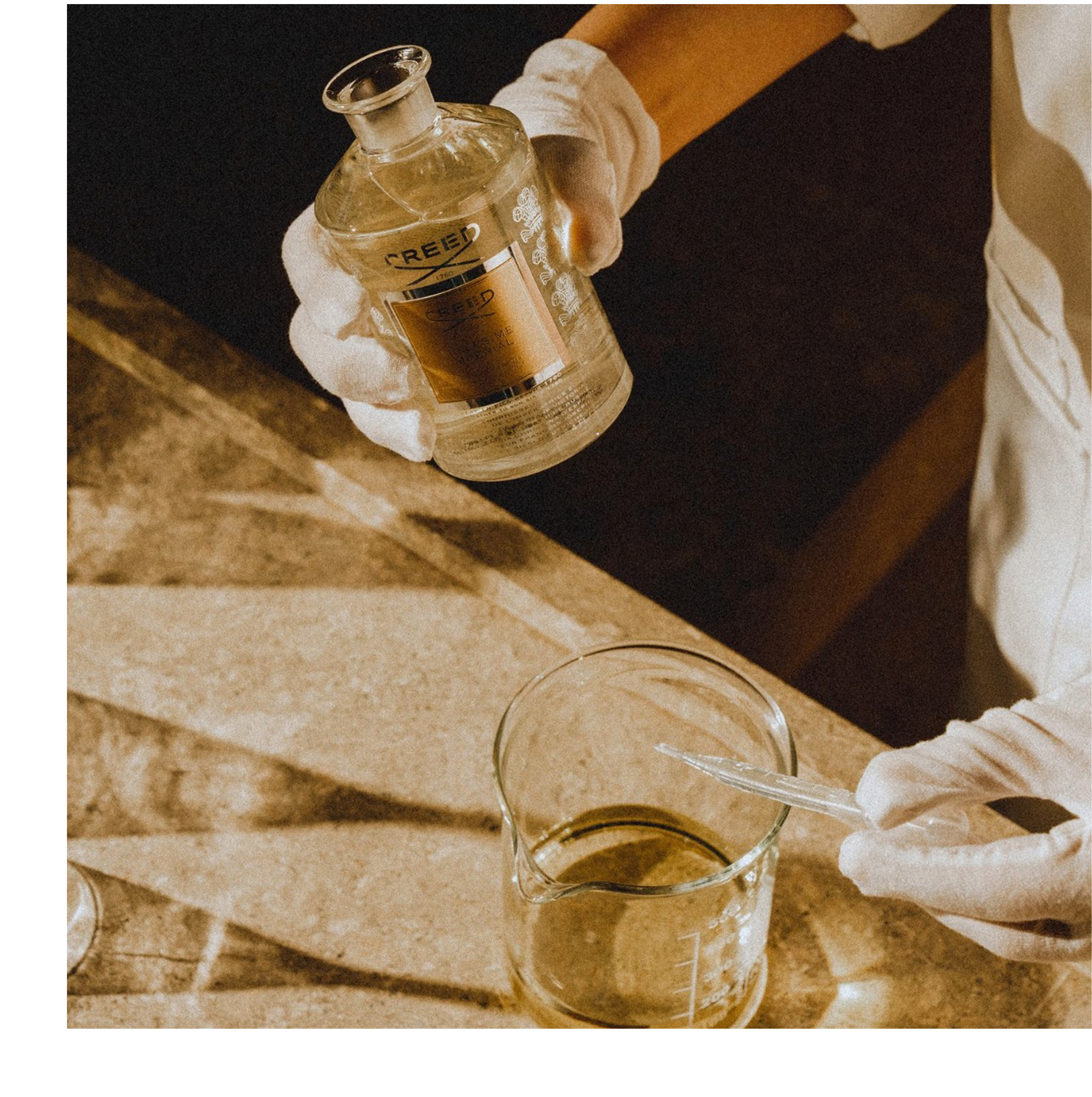 Person in white gloves holds a Creed bottle labeled CREED EAU DE PARFUM IMPERIAL above a beaker with a dropper.