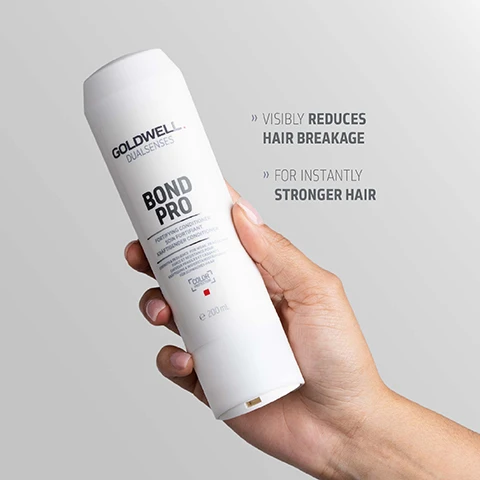 Image 1 - A hand holds a white Goldwell Dualsenses Bond Pro Fortifying Conditioner bottle, with text beside it reading Visibly reduces hair breakage For instantly stronger hair. Image 2 - A white Goldwell Dualsenses Bond Pro conditioner bottle stands on a light grey background with a swirl of white product next to its base, and the visible text reads GOLDWELL DUALSENSES BOND PRO FORTIFYING CONDITIONER SOIN FORTIFIANT KRÄFTIGENDER CONDITIONER INSTANT RESILIENCE FOR WEAK, FRAGILE HAIR RÉSILIENCE INSTANTANÉE POUR CHEVEUX FAIBLES ET FRAGILES SOFORTIGE WIDERSTANDSFÄHIGKEIT FÜR SCHWACHES, BRÜCHIGES HAAR COLOR PROTECTION 200 ML MICROPROTEC COMPLEX Innovative technology distributes essential care ingredients quickly and evenly for instant results you can see and feel. Image 3 - A white bottle of Goldwell Dualsenses Bond Pro Fortifying Conditioner is pictured against a blue background, displaying text that reads GOLDWELL DUALSENSES BOND PRO FORTIFYING CONDITIONER SOIN FORTIFIANT KRÄFTIGENDER CONDITIONER STRENGTHENS HAIR FOR VITAL STRONGER FEELING HAIR SOIN FORTIFIANT CAPILLAIRE POUR CHEVEUX FRAGILES ET CASSANTS KRÄFTIGENDE PFLEGE FÜR BRÜCHIGES HAAR COLOR PROTECTION e 200mL, with additional text below the bottle reading ClimatePartner certified product climate-id.com/PBNVQ3 and CO2 measure reduce contribute.