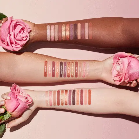 The image shows three arms of various skin tones that have colour swatches on them of each shade. Each hand holds a pink rose. Colours included are Saddle, Grapefruit, Claret, Mango, Deep Berry, Primrose, Fire Opal, Sparkling Amber, Rouge, Honey, Peony and Rose Water