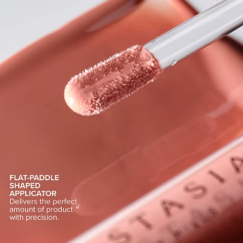 Image 2 - A close-up shows a flat paddle-shaped applicator for lip product coated in a light peach shade, held above a container with ANASTASIA visible, accompanied by the text FLAT-PADDLE SHAPED APPLICATOR Delivers the perfect amount of product with precision. Image 4 - The image displays two sections of cosmetic color swatches, Tinted Finish full-coverage matte color with no shimmer including Latte, Soft Pink, Deep Taupe, Sun Baked, Peachy Nude, Cotton Candy, Guava, Butterscotch, Caramel, Tan Rose, Dusty Rose, and Shimmer Finish full-coverage color with dazzling sparkle & metallic sheen including Honey Diamond, Amber Sparkle, Peachy, Goldy, Toffee Rose, Coral, Pink Ginger, Honey Kiss, and Cantaloupe. Image 5 - A single tube of nude shimmery lip gloss, shown both closed and with its applicator pulled out, resting on swatches of the product, accompanied by the text ANASTASIA BEVERLY HILLS HIGHLY-PIGMENTED, ULTRA-SMOOTH FORMULA WITH SEAMLESS GLIDE-ON HIGH-SHINE, NON-STICKY FINISH WITH COMFORTABLE WEAR LIGHT-REFLECTING SHADES IN TINTED + SHIMMER FINISHES. Image 6 - A close-up of a persons mouth shows a flat-paddle applicator applying clear lip gloss to the lower lip, with visible text reading: HOW TO APPLY Apply to the center of the top and bottom lip. Use the tip of the flat-paddle applicator to shape the lip line with precision. Image 7 - A person with glossy light pink lips is having a product applied to their lower lip with a clear applicator, and visible text reads PAIR WITH Lip Liner for a defined + sculpted look.
