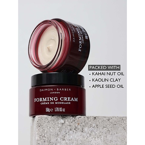 Image 3 - A stack of two red-brown Daimon Barber Forming Cream jars sits on a concrete block, with the top jar open revealing light cream inside, and text describing the product: DAIMON BARBER LONDON FORMING CREAM CRÈME DE MODELAGE 50g e 1.76 US oz PACKED WITH KAHAI NUT OIL KAOLIN CLAY APPLE SEED OIL.
