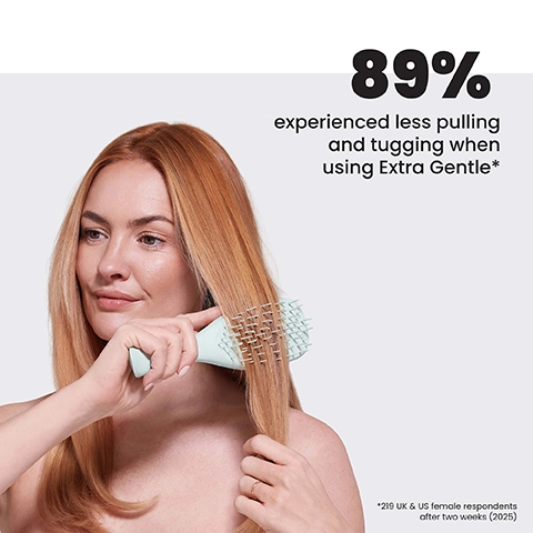 A woman with long reddish-blonde hair brushes it with a light green detangling brush, with text reading 89% experienced less pulling and tugging when using Extra Gentle* and *219 UK & US female respondents after two weeks (2025).