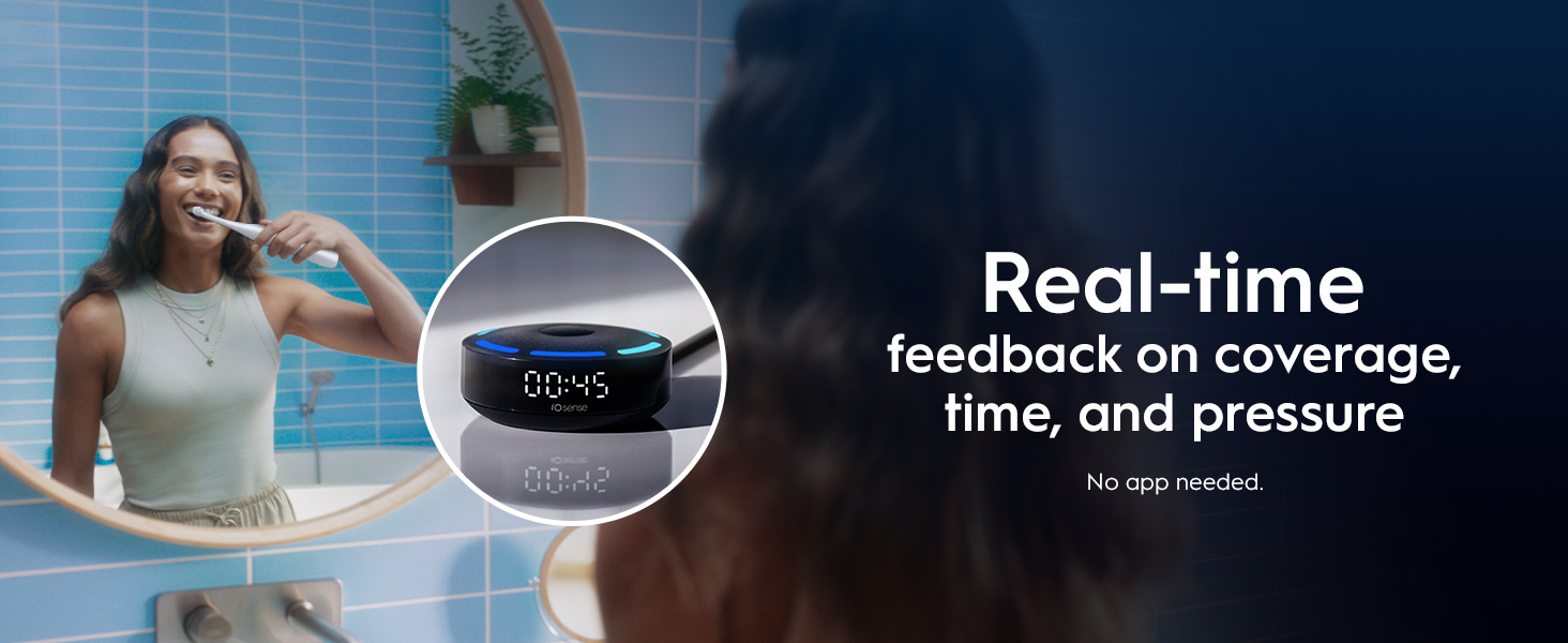 A woman smiles while brushing her teeth in a bathroom mirror reflection, next to a device displaying 00:45 and the text iO sense, with overlay text that reads Real-time feedback on coverage, time, and pressure No app needed.