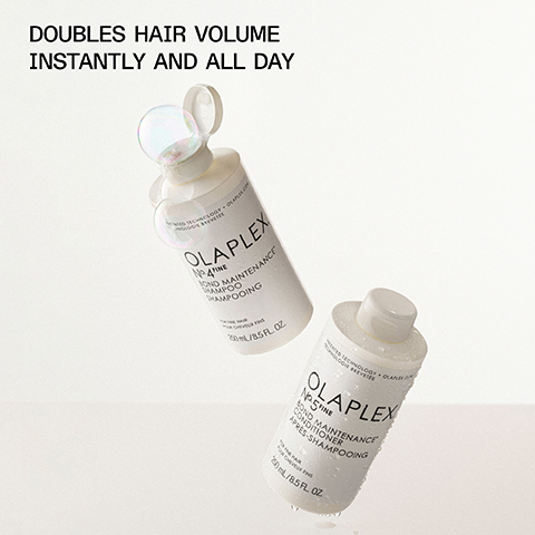 An image of two Olaplex hair care products, a shampoo bottle labeled Olaplex No. 4 Fine Bond Maintenance Shampoo and a conditioner bottle labeled Olaplex No. 5 Fine Bond Maintenance Conditioner, both appearing glossy with droplets of water and the text DOUBLES HAIR VOLUME INSTANTLY AND ALL DAY displayed above.