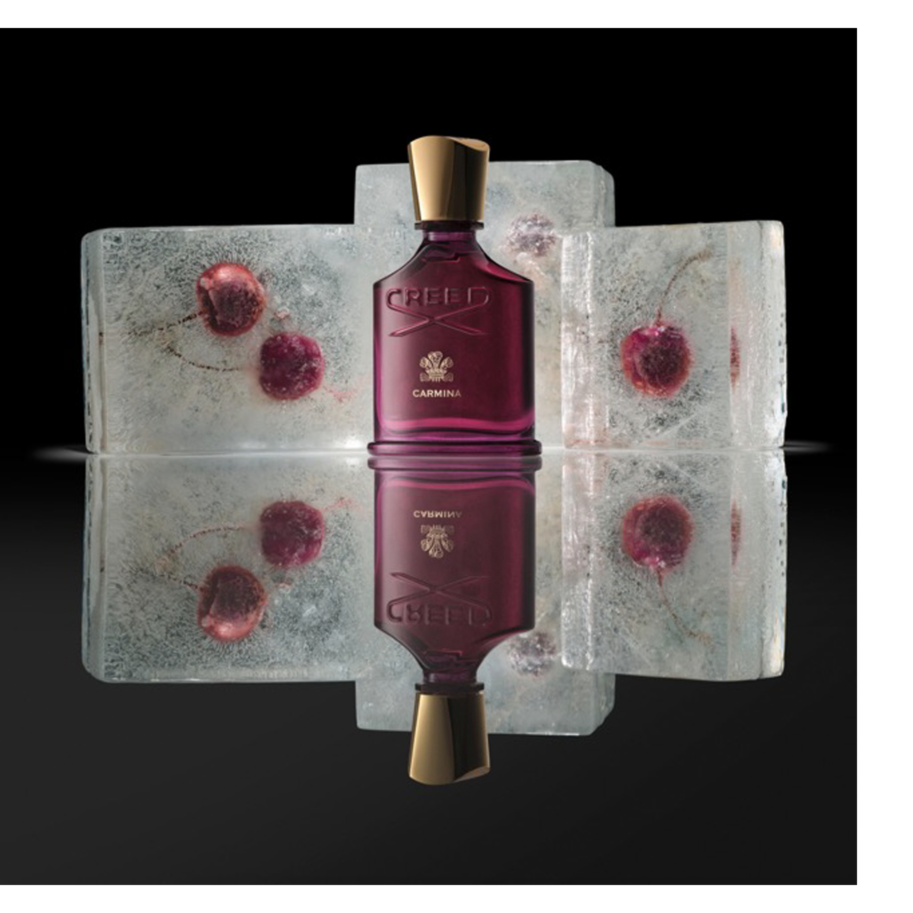 A dark magenta perfume bottle with a gold cap stands centered, flanked by two ice blocks with embedded red berries, all reflected on a glossy surface, and the bottle displays the text CREED and CARMINA.