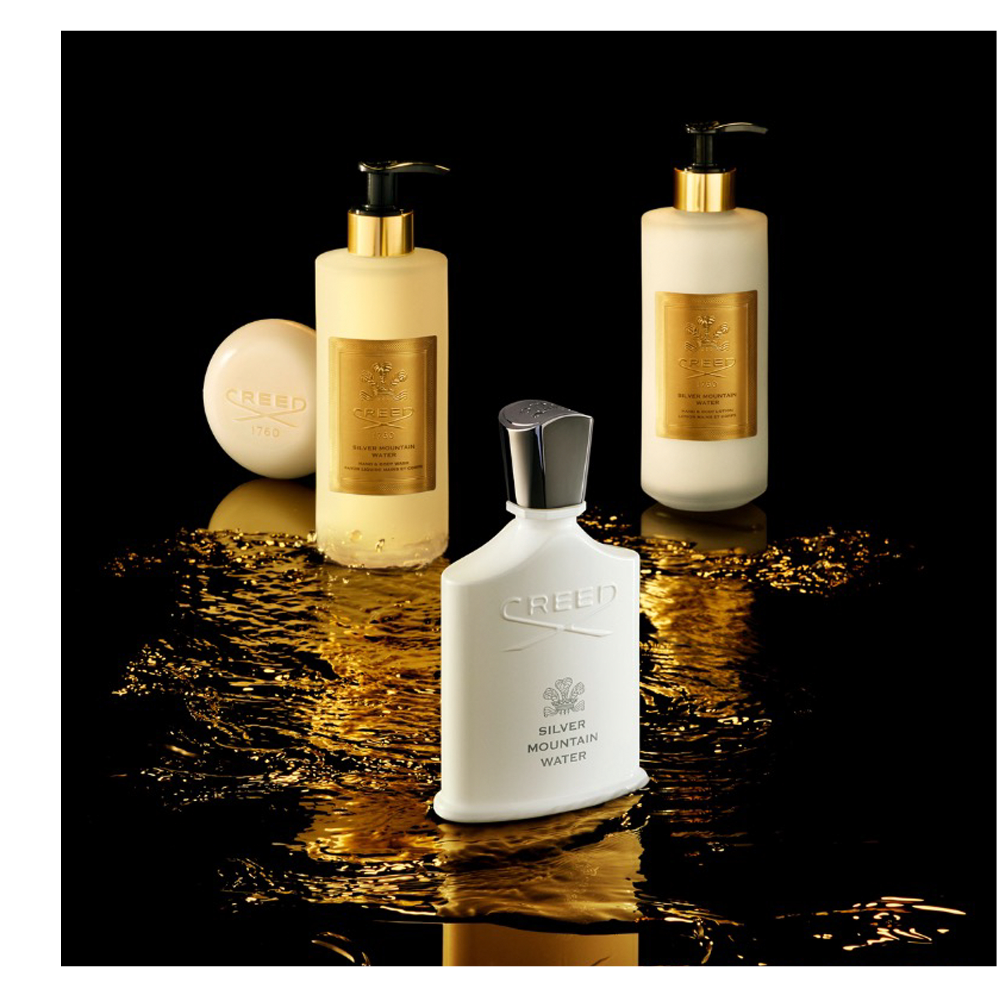 A black Creed perfume bottle, a cream-colored lotion bottle with a gold pump, and a round cream-colored bar of soap from the Green Irish Tweed line are displayed on a reflective black surface with shimmering gold liquid; the perfume bottle reads CREED, GREEN IRISH, TWEED, the lotion bottle reads CREED, 1760, GREEN IRISH TWEED, HAND & BODY WASH, SAVON LIQUIDE MAINS ET CORPS, and the soap reads CREED, 1760.