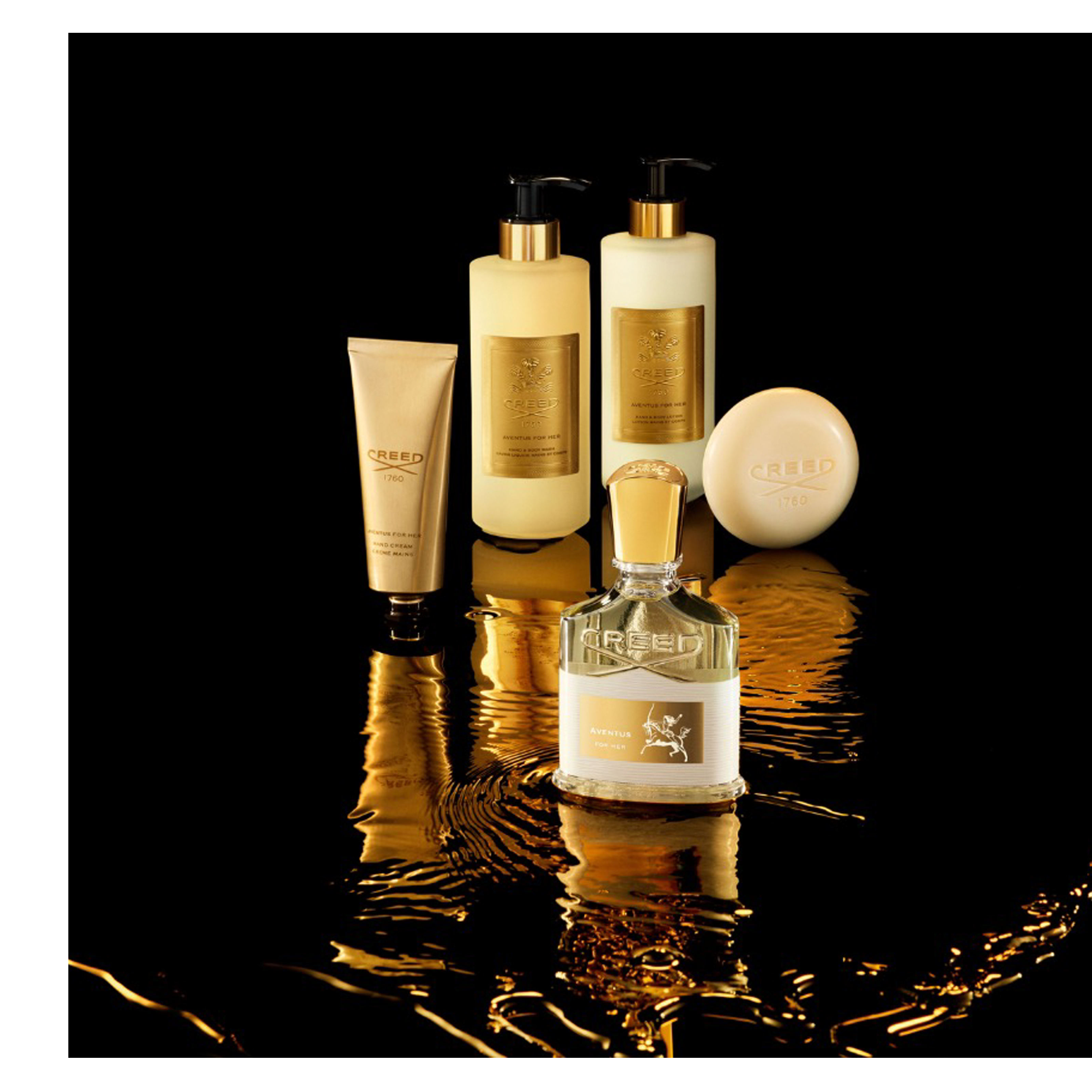 A collection of golden Creed Aventus For Her beauty products, including a perfume bottle, two pump bottles, a hand cream tube, and a bar of soap, rests on a black reflective surface with golden liquid swirls, prominently displaying the text Creed 1760, Aventus For Her, Savon Liquide Body Wash, Bain & Body Lotion, and Hand Cream.