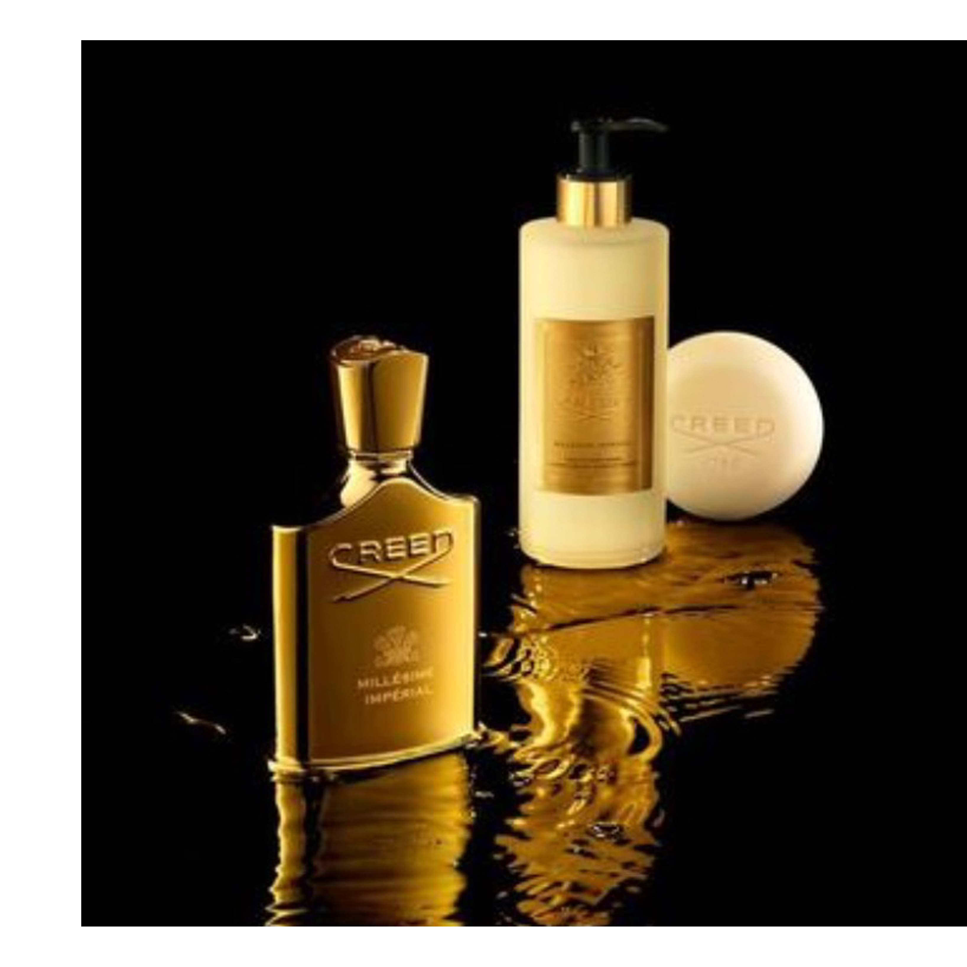 A golden Creed Millesime Imperial perfume bottle stands next to a cream lotion bottle with a black pump and a round cream Creed soap bar, all resting on a reflective surface with golden liquid splashes.