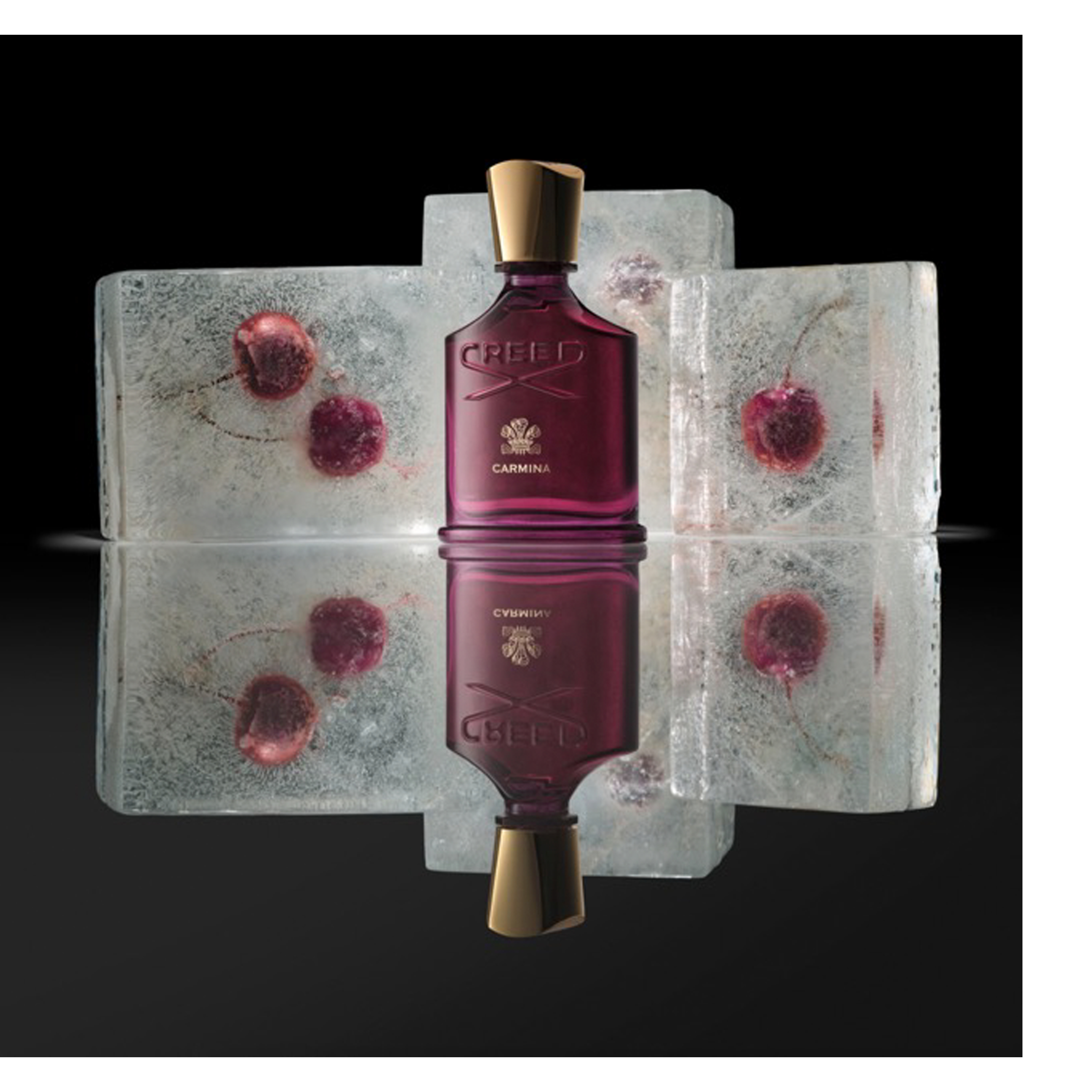 A deep red perfume bottle with a gold cap stands on a reflective surface against a dark background, flanked by four ice blocks containing red frozen cherries, with visible text CREED and CARMINA on the bottle.