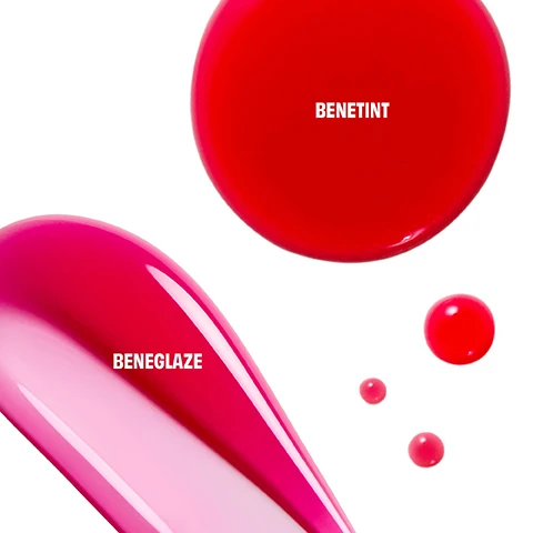 Image 2 - A red circular liquid swatch with the text BENETINT is at the top, while an elongated pink liquid swatch fading from dark to light pink with the text BENEGLAZE is at the bottom left, accompanied by three smaller pink liquid drops on a white background. Image 3 - The image displays two side-by-side beauty looks: on the left, a woman with rosy cheeks applies a red lip tint from a bottle labeled bene tint benefit, with the text BENETINT below; on the right, a woman with rosy cheeks and glossy red lips smiles, with the text BENETINT & BENEGLAZE below. Image 4 - A split image of a womans face shows her natural skin on the left with the text BEFORE, and on the right shows her with rosy blush and fuchsia lipstick with the text COMIN UP ROSES and Model is wearing shade Original Rose. Image 5 - A person with fair skin and dark hair applies a red lip tint to her lower lip with an applicator, holding the small bottle in her other hand, with text Benetint, Natural-looking flush, Longwearing, smudge-proof & transfer-proof, Sheer, buildable & lightweight, and Model is wearing Benetint Original. Image 6 - A woman demonstrates applying a red tint, first dotting it onto her cheek, then smiling as she applies it to her lips from a bottle labeled bene tint benefit, with instructions reading DOT ONTO CHEEKS & BLEND QUICKLY and GLIDE ONTO LIPS & LAYER TO BUILD INTENSITY. Image 7 - A smiling woman with rosy cheeks and bright fuchsia lips is shown in a close-up, with text that reads MODEL WEARS BENETINT SHADE | ORIGINAL. Image 8 - The image displays two Benefit Cosmetics full-size products on a white background: an open bottle of dark red liquid lip and cheek tint with its applicator, labeled bene tint benefit and FULL SIZE, and a closed tube of bright red lip gloss, labeled bene glaze benefit and FULL SIZE. Image 9 - A vibrant pink fluffy beauty bag with a wrist strap and textured indentations is shown, with a pink starburst in the corner announcing FREE BEAUTY BAG!