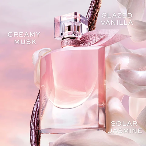 Image 1 - A pink perfume bottle with a clear lid and glittery bow is set against a soft pink and white background with flower petals and a dark pod, displaying the text Creamy Musk, Glazed Vanilla, Solar Jasmine. Image 2 - A person with dark skin holds a pink perfume bottle with a clear cap and a glittery pink ribbon, with the text A POWERFUL SKIN SCENT visible at the bottom. Image 3 - A pink perfume bottle with a pink bow is displayed inside a clear glass cloche on a stand, with the visible text LASTS ALL DAY LONG WITH EXCEPTIONAL 5-HOUR INTENSITY* and *SELF-ASSESSMENT TEST, 69 WOMEN. Image 4 - Julia Roberts smiles, wearing a white shirt, against a blurred sunset and city background, with the text La vie est belle VANILLE NUDE. Image 5 - The image displays four distinct perfume bottles with the title Find Your Perfect Scent, showing from left to right: Rose Extraordinaire Eau De Parfum in a pink bottle with a rose design, labeled as Bright Floral; New Vanille Nude Eau De Parfum in a light pink bottle with glitter, labeled as Musky Gourmand; LOriginal Eau De Parfum in an amber bottle with a grey ribbon, labeled as Gourmand Floral; and LElixir Eau De Parfum in a red bottle with black feathers, labeled as Velvety Floral.