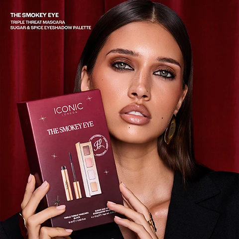 Image 2 - A woman with dark hair, prominent smokey eye makeup, and glossy lips holds a maroon gift box against a red velvet curtain; visible text in the image reads THE SMOKEY EYE TRIPLE THREAT MASCARA SUGAR & SPICE EYESHADOW PALETTE, and text on the box includes ICONIC LONDON THE SMOKEY EYE TRIPLE THREAT MASCARA BLACK 9 ml e / 0.30 fl.oz. SUGAR AND SPICE EYESHADOW PALETTE 4 x 1.9 g e / Net Wt. 0.06 oz. Image 3 - Three gold cosmetic products, including a mascara and an eyeshadow palette, are wrapped with a pink ribbon displaying the text ICONIC LONDON, with additional overlay text reading THE SMOKEY EYE, TRIPLE THREAT MASCARA, SUGAR & SPICE EYESHADOW PALETTE. Image 4 - Four customer review cards are displayed against a red curtain background, each featuring five stars and a testimonial: Triple Threat Mascara My favourite mascara, no clumping and makes my lashes look long, easy to remove. Like it so much brought as gifts! - Claire C; Sugar & Spice Eyeshadow Paletter I have 2 of these now. Loved the first one so much I bought another to keep in my handbag just in case. Long lasting and great colours. - Cathy p.; Triple Threat Mascara Hands down the best mascara Ive used and doesnt smudge or give you Panda eyes just love it! - Joanne S.; and Sugar & Spice Eyeshadow Paletter The colours are beautiful and each compliment the other if used together for a smouldering yet romantic look. Alternatively you can use the lighter colours for every day use at the office. - Sarah B. Image 5 - The image shows four cosmetic powder swatches in shades of light gold, reddish-brown, light peach, and shimmery taupe labeled Icon, Merlot Mondays, Taupe dTaupe, and Velvet Crush, next to a close-up of a mascara brush with black mascara creating a textured stroke, and the text Triple Threat Mascara, Volumises, Lengths, Lifts.
