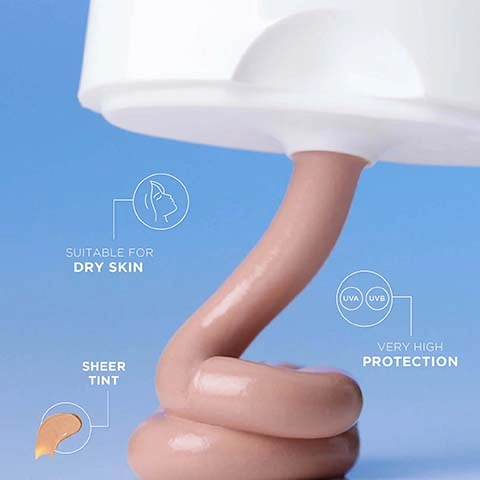 Image 2 - A thick stream of light brown tinted cream squeezes out from a white bottle against a blue background, displaying text that reads SUITABLE FOR DRY SKIN, SHEER TINT, UVA UVB, and VERY HIGH PROTECTION.
