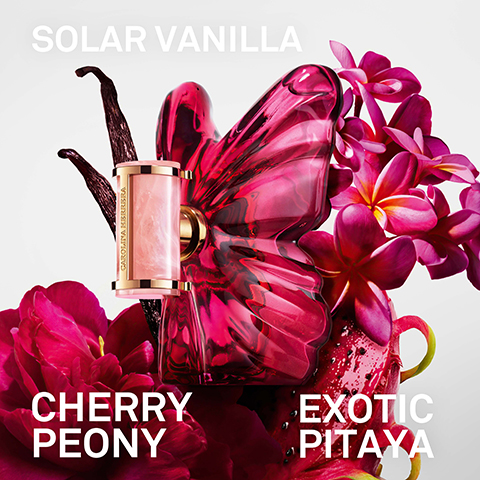 A pink butterfly-shaped perfume bottle with a small rectangular applicator, accompanied by vanilla beans, pink peonies, plumeria flowers, and a cut dragon fruit, with the text SOLAR VANILLA, CAROLINA HERRERA, CHERRY PEONY, EXOTIC PITAYA.