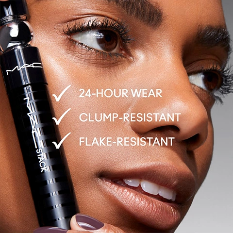 Image 5 - A close-up of a persons face with long eyelashes, holding a black MAC STACK mascara tube, next to three checked points that read 24-HOUR WEAR, CLUMP-RESISTANT, FLAKE-RESISTANT.