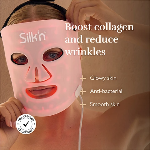 Image 2 - A person wears a pink LED face mask with red lights visible through the eye and mouth openings, with text that reads Silkn, Boost collagen and reduce wrinkles, Glowy skin, Anti-bacterial, Smooth skin, and a circular seal with a checkmark stating FDA CLEARED CE CERTIFIED. Image 3 - A pink Silkn face mask, with red light visible through its eye and mouth openings, lies on a textured table next to text that reads Results in just 2 weeks and Session time of 10 min. Image 4 - A four-panel image displays an LED light therapy mask illuminated in red, blue-white, yellow, and purple-pink light, with labels Anti-Aging, Reduces acne-related redness, Anti-Pigmentation, and Anti-Blemish. Image 5 - A woman wears a pink LED facial mask glowing red, with the text High effectiveness, Silkn®, and a light bulb icon followed by Irradiance between 13.5 - 74.9 mW/cm², LED light between 425 - 622nm.