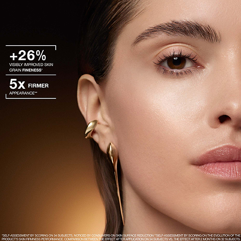 A close-up image of a womans face showing her eye, smooth cheek, and ear with golden earrings, accompanied by the text +26% VISIBLY IMPROVED SKIN GRAIN FINENESS*, 5X FIRMER APPEARANCE**, and *SELF-ASSESSMENT BY SCORING ON 34 SUBJECTS, NOTICED BY CONSUMERS ON SKIN SURFACE REDUCTION **SELF-ASSESSMENT BY SCORING ON THE EVOLUTION OF THE PRODUCTS SKIN FIRMNESS PERFORMANCE. COMPARISON BETWEEN THE EFFECT AFTER APPLICATION ON 34 SUBJECTS VS. THE EFFECT AFTER 2 MONTHS ON 32 SUBJECTS.