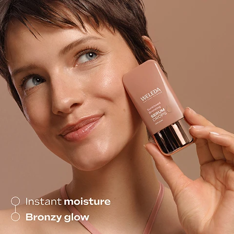 Image 3 - A young woman with short brown hair and blue eyes smiles softly, holding a Weleda Sunkissed Bronzing Serum Drops bottle to her radiant cheek; visible text on the bottle reads WELEDA NATURAL SCIENCE Sunkissed Bronzing SERUM DROPS with yuzu, and text below reads Instant moisture Bronzy glow. Image 4 - A split image features the top half with close-up yellow citrus slices in bubbly liquid and the bottom half with shimmering bronze glitter, accompanied by the text YUZU hydrates skin instantly and MINERAL PIGMENTS immediate bronzing effect. Image 5 - Three Weleda Serum Drops bottles are displayed against a brown background, illustrating a Sun-Kissed Glow Routine: a pink and green bottle for Slow Aging Astaxanthin with white tea, a bronzed bottle for Sunkissed Bronzing with yuzu, and a blue and pink bottle for Hyaluronic Moisture with snow mushroom, accompanied by text that reads Sun-Kissed Glow Routine, AM Slow Aging Astaxanthin & Sunkissed Bronzing Serum for a radiant, naturally bronzed glow, and PM Hyaluronic Moisture for perfectly moistured skin. Image 6 - A persons hands are shown with a white cream and brown liquid swirl in the open left palm, while the right hand hovers above it, next to text that reads: Application Use 2-3 drops pure or Mix with your face cream (e.g. Skin Food Nourishing Day Cream) Apply and boost effect! Image 7 - Close-up of a persons face with a blue eye and a swatch of bronzy serum on their cheek, featuring the text Lightweight bronzy serum. Image 8 - A three-panel image illustrates the application of bronzing serum, with the top left panel showing a hand squeezing a drop from a Weleda bottle, the top right panel displaying bronzing drops mixed with white cream on a palm, and the bottom panel featuring a finger blending the product onto a persons cheek; visible text includes Drop it! WELEDA NATURAL SCIENCE Sunkissed Bronzing SERUM DROPS with yuzu Mix it! Boost it!