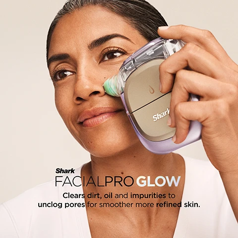 Image 1 - A woman with dark skin gently smiles as she uses a purple and gold Shark FacialPro Glow device with a green tip on the side of her nose, with text that reads Shark FACIALPRO GLOW Clears dirt, oil and impurities to unclog pores for smoother more refined skin. Image 2 - Close-up of a woman looking up as a hand applies a Shar skincare device to her cheek, with a purple circular graphic saying SPA LEVEL GLOW IN JUST 10 MIN, and text below stating Clinically tested to boost hydration +128% – in one use* followed by *Results from clinical study with 60 subjects immediate use of treatment. Individual results may vary. Image 3 - A man with dark skin applies a purple and gold skincare device to his cheek, with an inset showing his eye and a circular graphic depicting blue with a snowflake and red with wavy lines, accompanied by the text: INSTACHILL INSTAHEAT Shark DePuffi Helps contour the face and visibly depuff the under eyes for a brighter, more defined look. Image 4 - A woman smiles while applying a clear gel to her cheek with her hand, and an inset shows her holding a small white container of Shrunk The Detox 1, with the text DERM DETOX Supports spa-level exfoliation for clearer, cleaner pores. Image 5 - A light blue Shark brand HYDRO INFUSE bottle for Bio Hydration Hyaluronic Acid, 30mL, is featured on a light background with clear liquid droplets; a large droplet contains the text HYDRO INFUSE Hyaluronic Acid (HA) helps infuse skin with hydration for firmness and luminosity, and the bottle also reads Supplements for a Lasting Glow & Re-Energized Skin and 2.