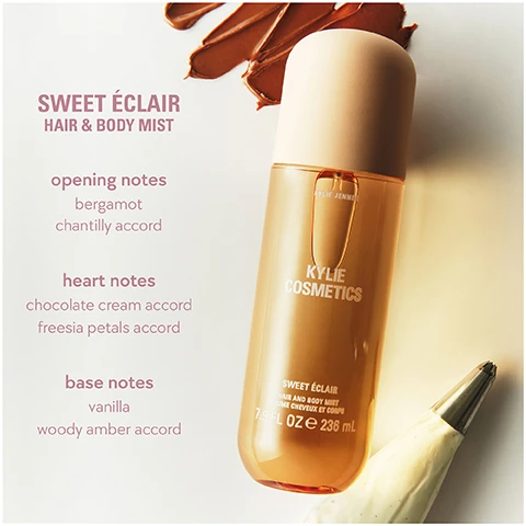 Image 1 - A golden-brown spray bottle of Kylie Cosmetics Sweet Éclair Hair & Body Mist is shown with smears of brown and a piping bag of frosting, featuring text listing opening notes bergamot chantilly accord, heart notes chocolate cream accord freesia petals accord, base notes vanilla woody amber accord, and on the bottle Kylie Jenner Kylie Cosmetics Sweet Éclair Hair and Body Mist Brume Cheveux et Corps 7.9 FL OZ e 236 mL. Image 2 - A silver spoon filled with dark brown chocolate ganache is positioned above a white bowl overflowing with white whipped cream, with text that reads a warm, chocolate, woody gourmand fragrance. Image 3 - Three Kylie Cosmetics hair and body mist bottles are displayed side by side, each labeled Kylie Jenner, Kylie Cosmetics, Hair and Body Mist / Brume Cheveux Et Corps, 7.9 FL OZ e 236 mL: the first bottle has a peach cap, an eclair graphic, and text Sweet Éclair velvety, warm, decadent; the second bottle has a light pink cap, a water lily graphic, and text Vanilla Dew creamy, milky, airy; and the third bottle has a cream cap, a caramel squares graphic, and text Caramel Cloud nutty, cozy, indulgent. Image 4 - A wavy gold perfume bottle with a dark round base is shown next to a tilted beige hair and body mist spray bottle on a light pink background, with text reading can be layered with another mist of the collection or a cosmic kylie jenner eau de parfum and the spray bottle is labeled KYLIE JENNER KYLIE COSMETICS VANILLA DEW HAIR AND BODY MIST BRUME CHEVEUX ET CORPS 7.9 FL OZ e 236 mL. Image 5 - Three clear bottles of Kylie Cosmetics mist, pink for Vanilla Dew, yellow for Caramel Cloud, and amber for Sweet Solaire, are displayed on a background transitioning from light to dark, with the visible text mists that take you from day to night, and on each bottle Kylie Jenner Kylie Cosmetics Hair and Body Mist Brume Cheveux et Corps 7.9 FL OZ e 236 mL. Image 6 - Three Kylie Cosmetics body mists are displayed on a light pink surface, featuring an upright yellow Vanilla Dew bottle, an upright pink Sweet Éclair bottle with its cap beside it, and an amber Caramel Cloud bottle lying on its side with its cap nearby, all labeled KYLIE COSMETICS 7.9 FL OZ / 236 mL, accompanied by scent layering recommendations: for a more indulgently sweet scent: layer sweet éclair over vanilla dew or caramel cloud; for a creamier, softer scent: layer vanilla dew over sweet éclair or caramel cloud; for a nuttier, richer scent: layer caramel cloud over vanilla dew or sweet éclair.