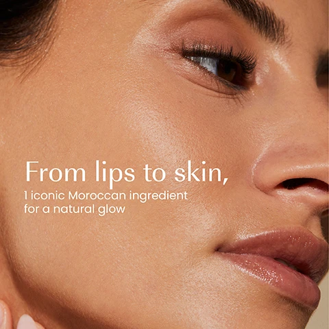 Image 1 - A close-up of a persons face with glowing skin, long eyelashes, and glossy lips, with text that reads From lips to skin, 1 iconic Moroccan ingredient for a natural glow. Image 2 - A hand holds a teal cosmetic jar, with a finger scooping a light peach cream out of it, displaying the text Evens skin tone, Defines lips, Naturally tints, Smooths lip lines, IZIL AKER FASSI & HA LIGHTWEIGHT GLOW CREAM, HYDRATE, STRENGTHEN SKIN BARRIER & GLOW, CRÈME LÉGÈRE ÉCLAT & BARRIÈRE FA & HA, كريم الإشراق الخفيف بالعكر الفاسي و حمض الهيالورونيك. Image 3 - A collection of Izil skincare products including a lip balm, daily cleanser, glow toner, lightweight glow cream, brightening face mask, gentle glow serum, and body scrub, displayed on stone blocks with natural elements like red flowers, prickly pear, and pomegranate, with visible text reading Nourish, Exfoliate, Tone, Moisturise, Mask, Naturally Tint, Scrub, IZIL Aker Fassi & Prickly Pear Nourishing Lip Balm, All Skin Types, IZIL ARA & Algae Exfoliating Daily Cleanser, Even Skin Tone Polish & Glow, With White Flower, Red Algae, ALL SKIN TYPES, NETTOYANT DE VISAGE EXFOLIANT QUOTIDIEN, IZIL AKER FASSI & RICE PROTEIN GLOW TONER, PORE MINIMIZER BRIGHTENING SKIN & HEALTHY RADIANCE, TONIFIANT ÉCLAT & UNIFORMISANT, IZIL AKER FASSI & VIT C LIGHTWEIGHT GLOW CREAM, HYDRATING BRIGHTENING & ANTI AGING, IZIL AKER FASSI BRIGHTENING FACE MASK, Detoxifying & Purifying, IZIL AKER FASSI & VIT C GENTLE GLOW SERUM, IZIL AKER FASSI & POMEGRANATE BRIGHTENING BODY SCRUB, Exfoliating & Smoothing, ALL SKIN TYPES.