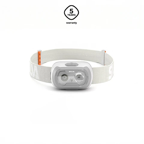 Image 1 - A white and grey headlamp with a white strap is displayed, featuring a 5-year warranty badge, and visible text SILVA, 500 LM, MODE, 5 YEARS warranty. Image 2 - An open white battery compartment with slots for three AAA batteries is next to a black rechargeable battery pack labeled SILVA with CHARGING and CHARGED indicators, and three silver AAA batteries labeled AAA with plus and minus symbols; a graphic in the top right corner displays a stylized H logo and the text Hybrid technology. Image 3 - A close-up shows a grey headlamp strap with a white and grey lamp head featuring the SILVA logo, and an orange and white adjuster; text in the upper right corner reads INTEGRATED CLIP Seek comes with a detachable lamp head, with multiple attachment options. Image 4 - Three dark, wall-mounted lights illuminate beams of increasing brightness from left to right, along with the text 3 brightness levels.