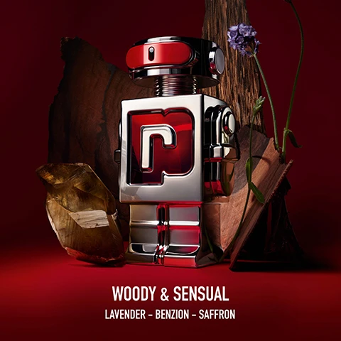 Image 1 - A silver and red robot-shaped perfume bottle with a prominent red P on its chest stands amidst pieces of wood, a raw crystal, and a lavender flower against a dark red background, with the text Woody & Sensual and Lavender - Benzoin - Saffron below. Image 2 - The image shows four robot-shaped Phantom perfume bottles displayed horizontally, each with different liquid colors and background elements, along with descriptive text: PHANTOM EAU DE TOILETTE SENSUAL & FRESH, PHANTOM INTENSE EAU DE PARFUM INTENSE POWERFUL & AROMATIC, PHANTOM PARFUM ADDICTIVE & WOODY, PHANTOM IN RED PARFUM ELIXIR WOODY & SENSUAL, and a horizontal intensity scale at the bottom from + FRESH to + INTENSE.