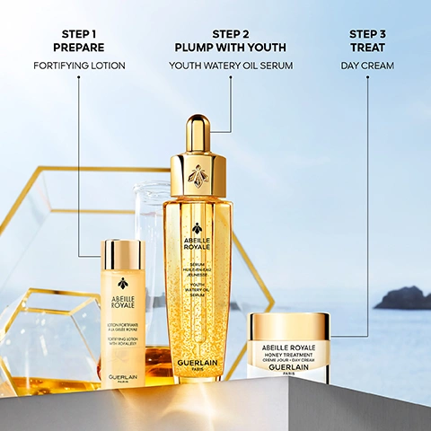 Image 1 - Three gold and white Guerlain Abeille Royale skincare products, a fortifying lotion, a youth watery oil serum, and a day cream, are displayed on a reflective surface against a blurred outdoor background, with visible text reading Step 1 Prepare Fortifying Lotion, Step 2 Plump With Youth Youth Watery Oil Serum, Step 3 Treat Day Cream, Abeille Royale Lotion Fortifiante à la Gelée Royale Fortifying Lotion with Royal Jelly Guerlain Paris, Abeille Royale Sérum Huile-en-eau Jeunesse Youth Watery Oil Serum Guerlain Paris, and Abeille Royale Honey Treatment Crème Jour Day Cream Guerlain Paris. Image 2 - Close-up of a woman with clear skin touching her cheek against a blue background, with text that reads Skin Dehydration Is Reduced By: -20%¹, Fortifying Lotion, and Instrumental test, single application by 11 volunteers, results after 24 hours. Image 3 - A close-up of a woman with radiant skin, wearing a white top and honeycomb earrings, holding a gold serum bottle, with text on the image reading AFTER 1 MONTH EVALUATED BY PANEL¹: SMOOTHER +48% FIRMER +53% MORE ELASTIC +56% YOUTH WATERY OIL SERUM, and the bottle is labeled Guerlain Abeille Royale Sérum Huile En Eau Jeunesse Youth Watery Oil Serum, with a small disclaimer at the bottom stating ¹Self-scoring, test 40 women, 2 applications per day. Image 4 - A woman with clear skin holds a jar of Guerlain Abeille Royale Honey Treatment Day Cream against a blue sky background, with text reading DERMATOLOGICAL SCORAGE¹ WRINKLES -48% FIRMNESS +57% SMOOTHNESS +98% RADIANCE +63% DAY CREAM ¹Clinical test by an independent dermatologist, 33 women, Europe, once a day, results after 1 month. Image 5 - A person in a white beekeeper suit with GUERLAIN PARIS visible on it stands on a rocky, flower-covered cliff overlooking the ocean at sunset, next to a wooden beehive marked with GUERLAIN, with additional text overlaid that reads Since 2011, Guerlain has been a patron of the Association of the Ouessant Island Brittany Black Bee Conservatory (ACANB), supporting bee protection and scientific research.