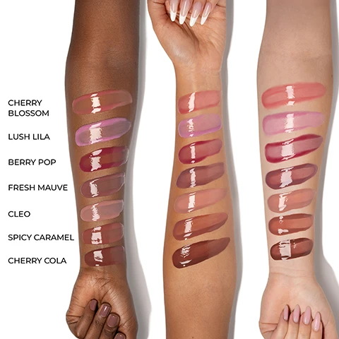 Image 1 - Three arms with varying skin tones display seven glossy lip product swatches in shades of pink, berry, mauve, and brown, labeled Cherry Blossom, Lush Lila, Berry Pop, Fresh Mauve, Cleo, Spicy Caramel, and Cherry Cola. Image 2 - Grid displaying seven rows of lip gloss swatches and applications on models with different skin tones, including shades Cherry Blossom, Lush Lila, Berry Pop, Fresh Mauve, Cleo, Spicy Caramel, and Cherry Cola. Image 3 - An image displays a pink lip gloss tube and applicator with a gloss swatch, alongside text promoting HY-GLOSS HY-BRID Tinted Gloss Balm, stating SHINE OF A GLOSS & COMFORT OF A BALM, Glassy Wet Shine Finish, Medium color payoff, Buttery, Cushiony feel, and Non-Sticky, with Natasha Denona visible on the tube. Image 4 - A pink lip gloss applicator is centered on a white background with product information: HY-GLOSS HY-BRID Tinted Gloss Balm, featuring an image of a raspberry with the text Raspberry Plant Cells, an image of a white rose with the text White Tea Rose Cells, and benefits listed as IMMEDIATE & LONG-TERM HYDRATION, HYALURONIC ACID & CERAMIDE PRODUCTION, SMOOTHES THE LIPS, and STRENGTHENS COLLAGEN & ELASTIN ENZYMES.