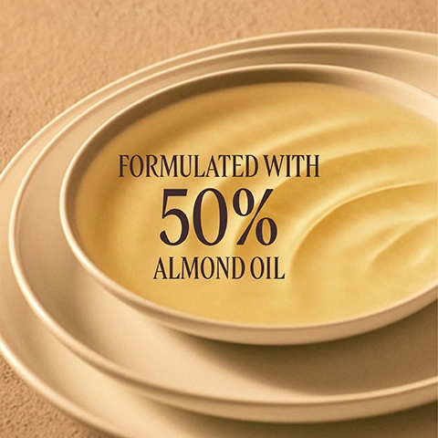 Image 3 - A light yellow, creamy substance is in a white bowl, with other bowls stacked underneath, against a textured background, with the text Formulated with 50% Almond Oil. Image 4 - A woman with glowing skin, wearing a white shirt, is touching her legs, with text superimposed that reads -44% STRETCH MARKS APPEARANCE* *Clinical scoring of stretch marks color on 21 women after 8 weeks.