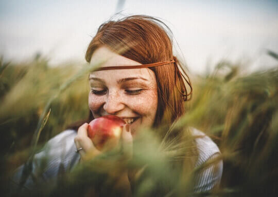 Une femme qui mange une pomme rouge dans un champ