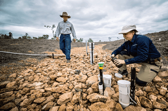 Image of a man standing and woman kneeling pouring liquid in a cup near the reef