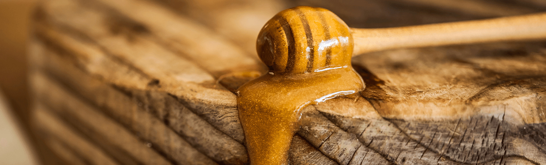 A wooden honey dipper laying on a wooden table and manuka honey slowly flowing down the table.